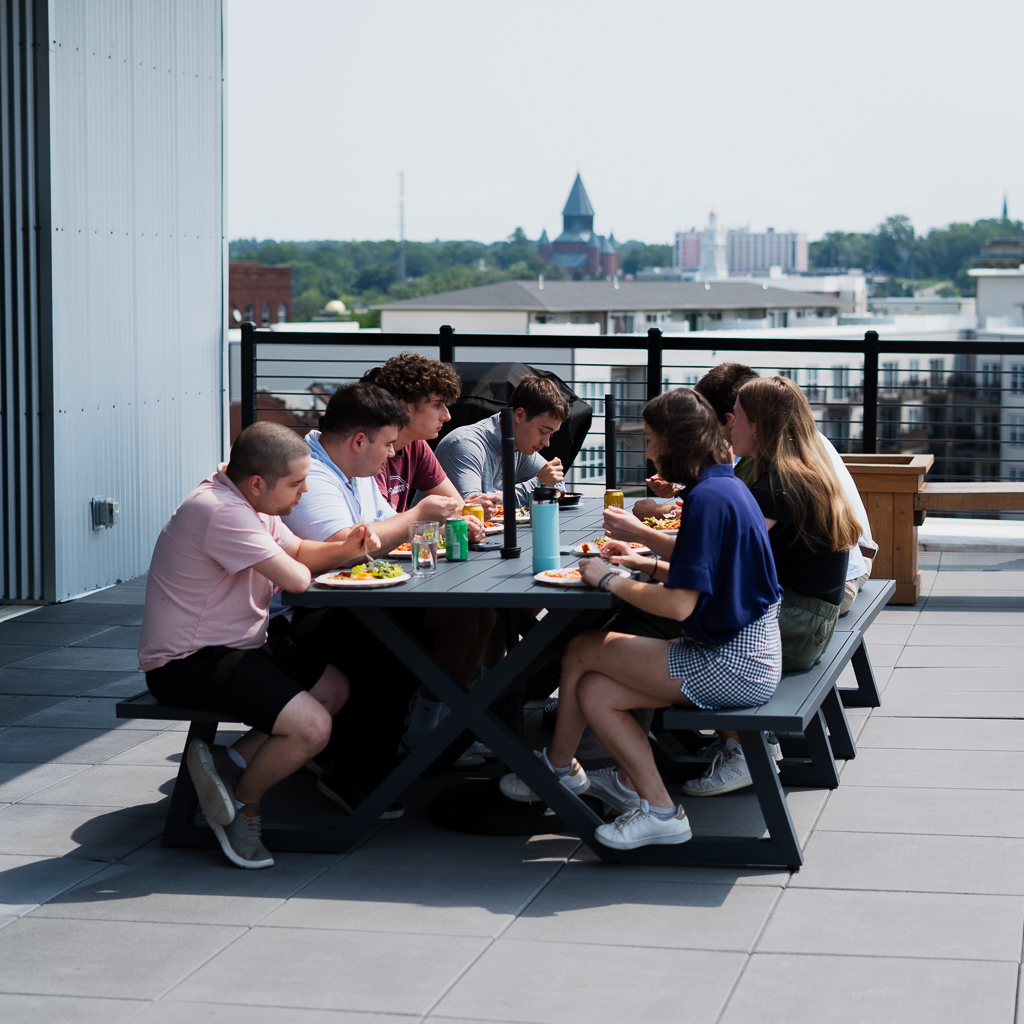 The team eating lunch at a long table on the Jahnel Group rooftop patio, Schenectady skyline behind